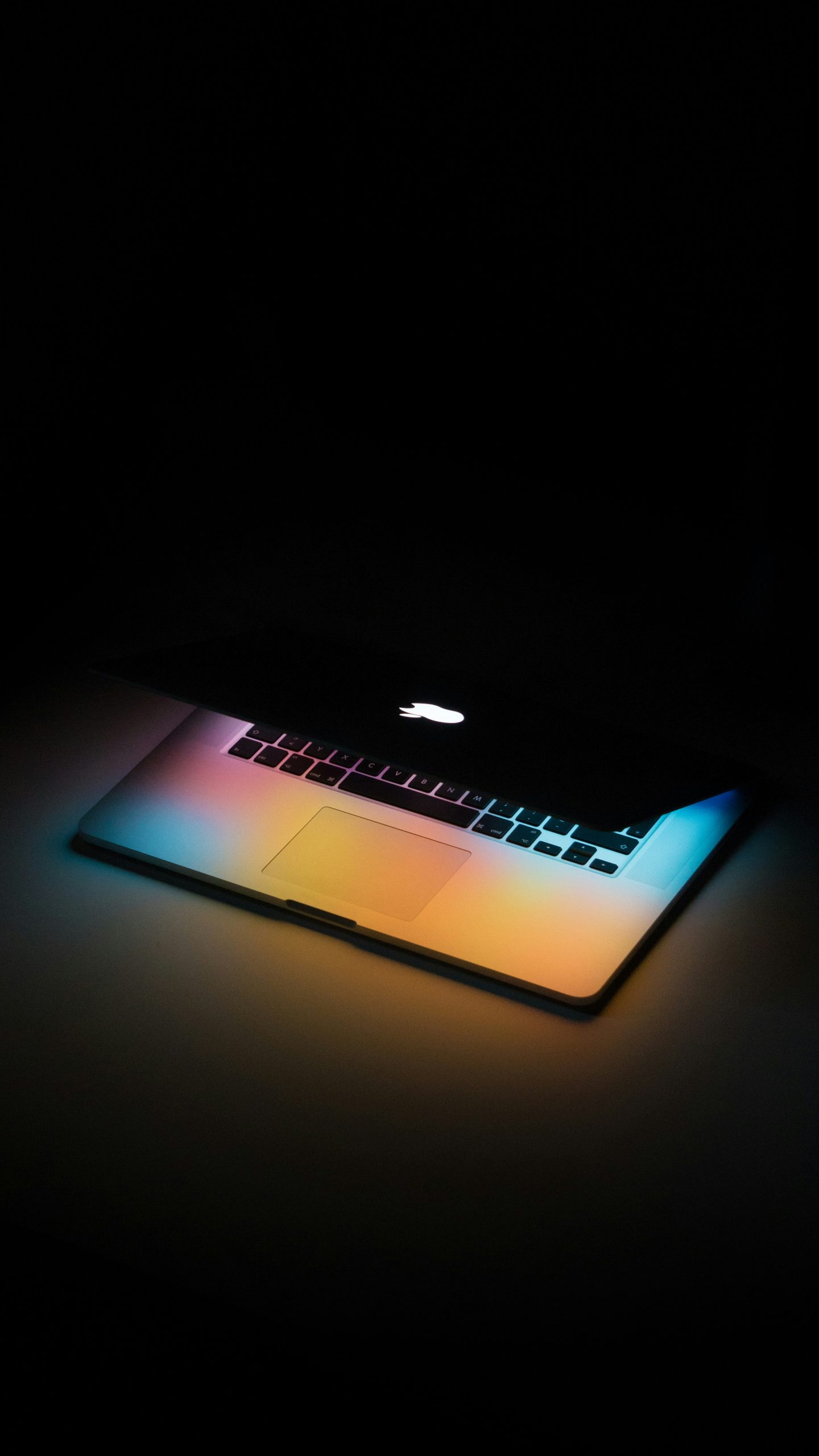 ein Macbook in einer dunklen Umgebung. Es ist leicht aufgeklappt und wirft farbiges Licht vom Bildschirm ab.